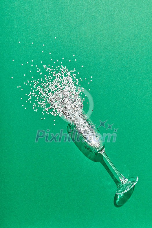 Christmas bright decoration in a glass as a champagne alcohol drink with shadows on green background with place for text. Greeting holiday card. Christmas bright decoration in a glass as a champagne alcohol drink with shadows on green background with place for text. Greeting holiday card.