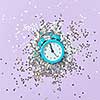Christmas background with twelve hours on a blue alarm clock and bright silver tinsel on a lavender paper, copy space. Holiday card.