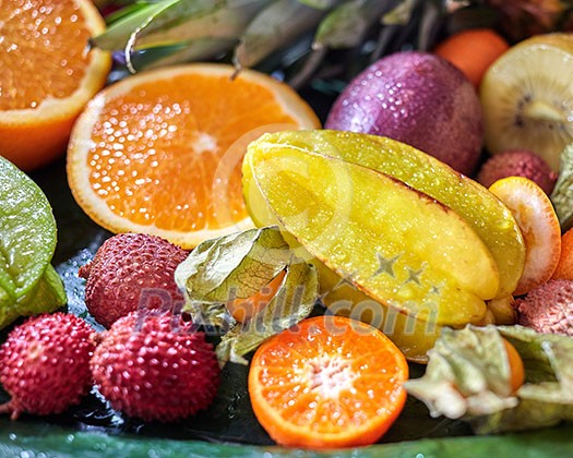 Jicy fresh tropical fruits as a backgraund. Passion fruit, carambola, litchi, kumquat, orange halves, phisalis on a green leaves. Close-up. Top view. Jicy fresh tropical fruits as a backgraund. Passion fruit, carambola, litchi, kumquat, orange halves, phisalis on a green leaves. Close-up. Top view.