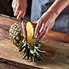 Woman's hands with a knife cut a juicy pineapple on a wooden board on a brown table around a dark background. Healthy ingredient
