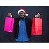 Indian  man wearing party clothes in Santa hat with shopping bag on dark  background studio dark skinned middle eastern Santa Claus merry Christmas