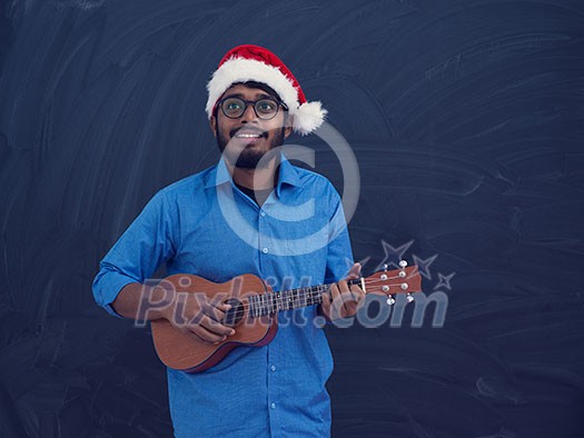 Indian man wearing Santa Claus Christmas red hat and playing Latin America traditional small guitar Indian man wearing Santa Claus Christmas red hat and playing Latin America traditional small guitar