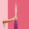 Woman's hand holds painted champagne bottle with holiday firecracker on a duotone pink background, copy spase. Christmas concept.