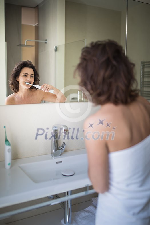 Pretty, middle aged woman brushing her teeth in a modern design bathroom Pretty, middle aged woman brushing her teeth in a modern design bathroom