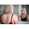 Pretty, middle aged woman brushing her teeth in a modern design bathroom