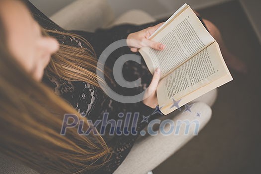 Cute young woman reading a book in a designer chair - color toned image, shallow DOF