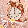 Close up golden painted alarm clock with Christmas time is midnight on a shiny golden abstract background with lights garland, copy space.