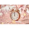 Golden alarmclock with time is midnight on a shiny golden abstract background with string of lights. Greeting card.