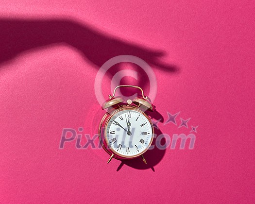 Retro cooper alarm clock with hard shadows from woman's hand on a hot pink background, copy space. Retro cooper alarm clock with hard shadows from woman's hand on a hot pink background, copy space.