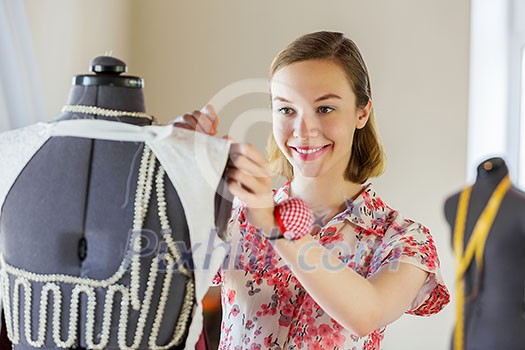 Pretty dressmaker at work pinning dress on dummy Pretty dressmaker at work pinning dress on dummy