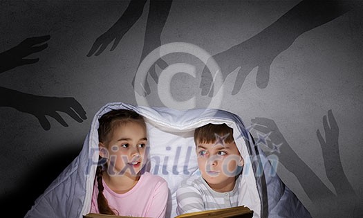 Children sitting in bed under blanket with book Children sitting in bed under blanket with book