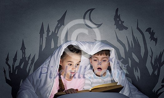Children sitting in bed under blanket with book Children sitting in bed under blanket with book