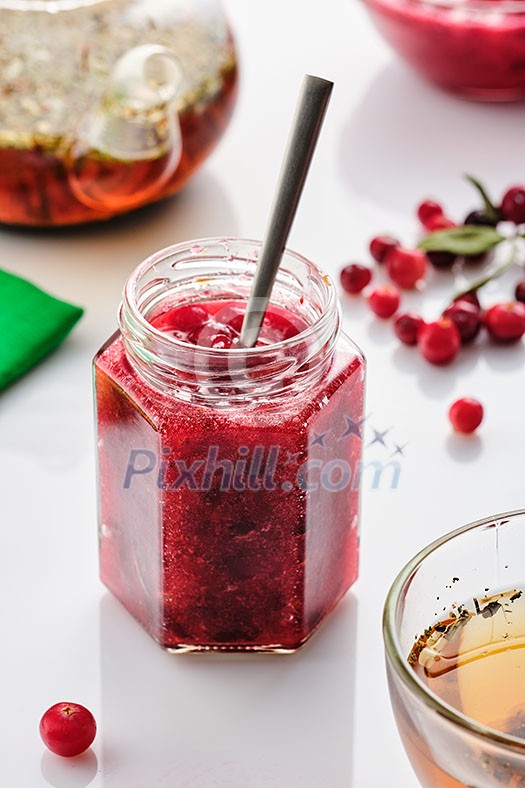 Cranberry jam in a glass jar and teapot on a white background Cranberry jam in a glass jar and teapot on a white background