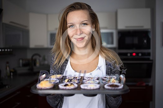 Pretty, young woman baking gluten free cupkes - taking them out of the oven, being pleased with the result Pretty, young woman baking gluten free cupkes - taking them out of the oven, being pleased with the result