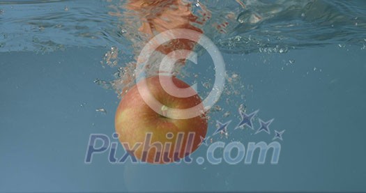 Slowly falling of fresh organic juicy apple with splashing into glass water aquarium on a grey background. Slow motion 2K video. Slowly falling of fresh organic juicy apple with splashing into glass water aquarium on a grey background. Slow motion 2K video.