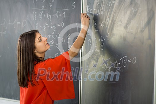 Pretty, young college student/young teacher writing on the chalkboard/blackboard during a math class Pretty, young college student/young teacher writing on the chalkboard/blackboard during a math class