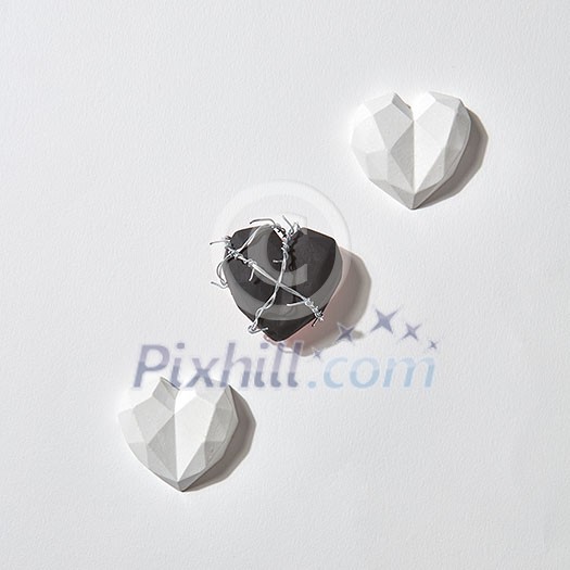 Greeting Valentine's card with three plaster hearts on a light gray background with shadows and copy space. One of them is black and wrapped twisted wire. Holiday concept. Greeting Valentine's card with three plaster hearts on a light gray background with shadows and copy space. One of them is black and wrapped twisted wire. Holiday concept.