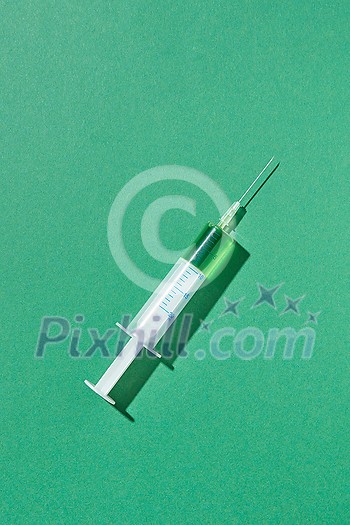 Green vaccine or serum in plastic syringe 20 ml for an intravenous injection on a light green background with hard shadow, copy space. Green vaccine or serum in plastic syringe 20 ml for an intravenous injection on a light green background with hard shadow, copy space.