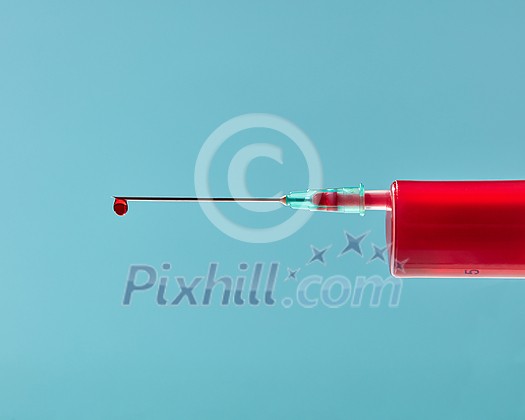 Red liquid or blood in plastic syringe with droplet on the needle on a pastel blue background, copy space. Red liquid or blood in plastic syringe with droplet on the needle on a pastel blue background, copy space.