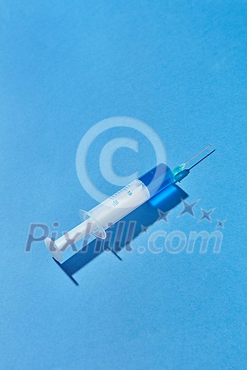Blue serum or vaccine in plastic syringe 20 ml for an intravenous injection on a pastel blue background with hard shadow, copy space. Blue serum or vaccine in plastic syringe 20 ml for an intravenous injection on a pastel blue background with hard shadow, copy space.