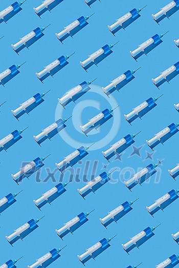Vertical healthcare pattern from sterile plastic syringes with blue injectable drugs or vaccine for injections on a pastel blue background, hard shadows. Top view. Vertical healthcare pattern from sterile plastic syringes with blue injectable drugs or vaccine for injections on a pastel blue background, hard shadows. Top view.