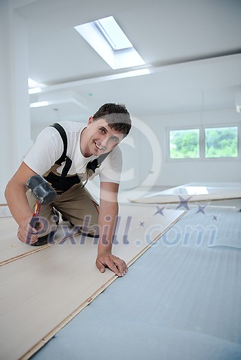 professional carpenter using rubber hammer while installing new laminated wooden floor in a unfinished apartment professional carpenter using rubber hammer while installing new laminated wooden floor in a unfinished apartment