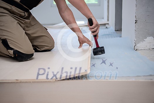 professional carpenter using rubber hammer while installing new laminated wooden floor in a unfinished apartment professional carpenter using rubber hammer while installing new laminated wooden floor in a unfinished apartment