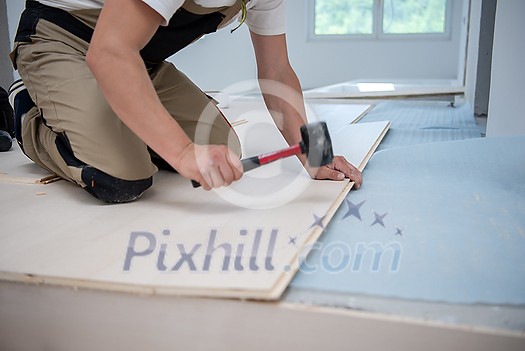 professional carpenter using rubber hammer while installing new laminated wooden floor in a unfinished apartment professional carpenter using rubber hammer while installing new laminated wooden floor in a unfinished apartment