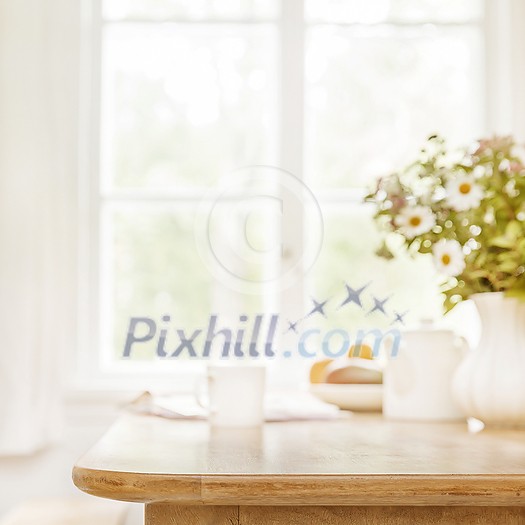 Home wooden kitchen table top with focus in front and blurred background showing breakfast tablewear, windowframe and a vase filled with garden flowers. Space for text. Home wooden kitchen table top with focus in front and blurred background showing breakfast tablewear, windowframe and a vase filled with garden flowers. Space for text.