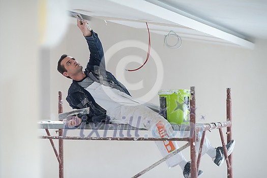 young professional construction worker using scaffold while plastering on gypsum ceiling inside the new big modern two levels apartment young professional construction worker using scaffold while plastering on gypsum ceiling inside the new big modern two levels apartment