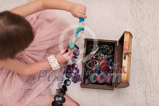 beautiful cute little girl in pink dress enjoying while playing with mother's jewelry from box on the floor at home beautiful cute little girl in pink dress enjoying while playing with mother's jewelry from box on the floor at home