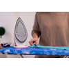beautiful young red haired housewife in good mood ironing clothes on ironing board in front of a white wall at home