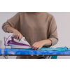 beautiful young red haired housewife in good mood ironing clothes on ironing board in front of a white wall at home