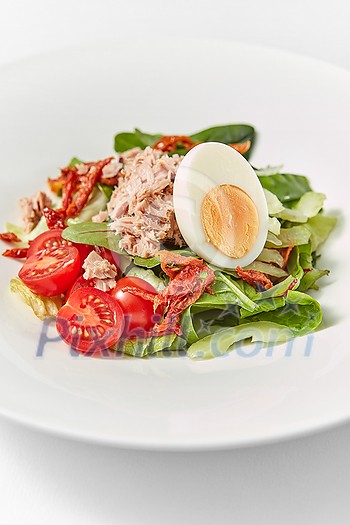 Freshly cooked delicious homemade tuna salad with fresh natural organic vegetables, tomatoes, spinach and half of egg on a white ceramic plate, copy space. Freshly cooked delicious homemade tuna salad with fresh natural organic vegetables, tomatoes, spinach and half of egg on a white ceramic plate, copy space.