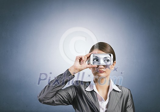 Beautiful young woman holding mobile phone against her eyes Beautiful young woman holding mobile phone against her eyes