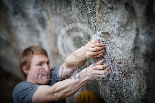 A rock climber climbing on a boulder rock outdoors. Group of friends involved in sports outside. A rock climber climbing on a boulder rock outdoors. Group of friends involved in sports outside.