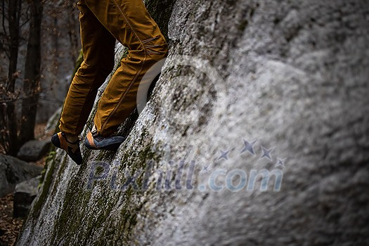 A rock climber climbing on a boulder rock outdoors. Group of friends involved in sports outside. A rock climber climbing on a boulder rock outdoors. Group of friends involved in sports outside.