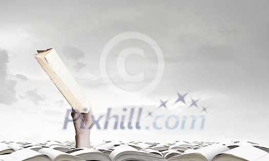Hand with book reaching out from pile of old books Hand with book reaching out from pile of old books