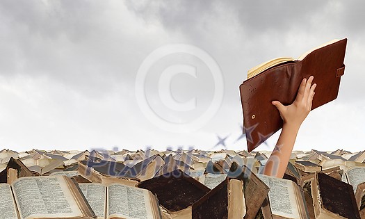 Hand with book reaching out from pile of old books Hand with book reaching out from pile of old books