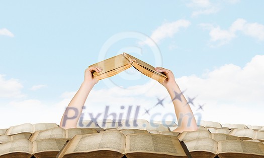 Hand with book reaching out from pile of old books Hand with book reaching out from pile of old books