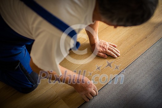 DIY, repair, building and home concept - close up of male hands lying parquet floor board/laminate flooring (shallow DOF; color toned image)