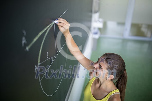 Cute female university/highschool student in class at the blackboard during math class Cute female university/highschool student in class at the blackboard during math class