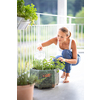 Pretty, young woman watering herbs she is growing on her balcony.