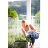 Pretty, young woman watering herbs she is growing on her balcony.