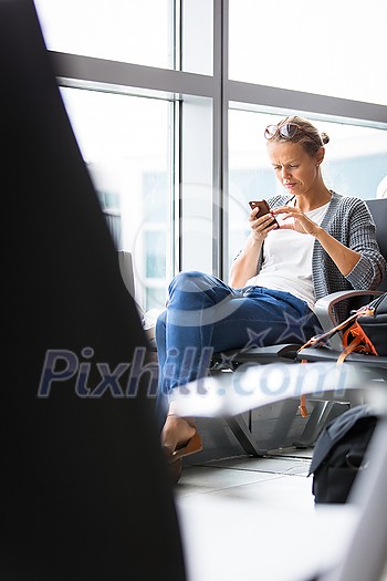Casual blond young woman using her cell phone while waiting to board a plane at departure gates at international airport. Casual blond young woman using her cell phone while waiting to board a plane at departure gates at international airport.