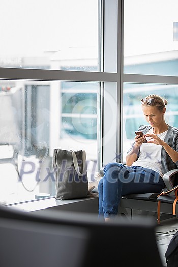 Casual blond young woman using her cell phone while waiting to board a plane at departure gates at international airport. Casual blond young woman using her cell phone while waiting to board a plane at departure gates at international airport.
