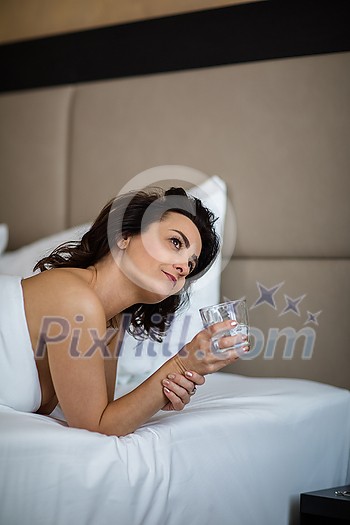 Beautiful young woman drinking water in bed first thing in the morning Beautiful young woman drinking water in bed first thing in the morning