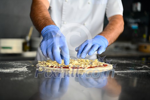 Skilled chef preparing traditional italian pizza in interior of modern restaurant kitchen with special wood-fired oven. Wearing protective medical face mask and gloves in coronavirus new normal concept Skilled chef preparing traditional italian pizza in interior of modern restaurant kitchen with special wood-fired oven. Wearing protective medical face mask and gloves in coronavirus new normal concept