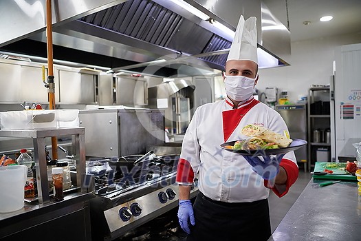 chef cook wearing face protective medical mask for protection from corona virus disease with plate of authentic sandwich at professional restaurant kitchen. Health, safety and pandemic concept in new normal concept chef cook wearing face protective medical mask for protection from corona virus disease with plate of authentic sandwich at professional restaurant kitchen. Health, safety and pandemic concept in new normal concept
