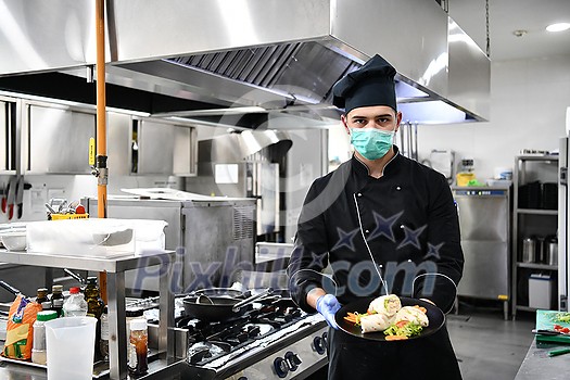 chef cook wearing face protective medical mask for protection from corona virus disease with plate of authentic sandwich at professional restaurant kitchen. Health, safety and pandemic concept in new normal concept chef cook wearing face protective medical mask for protection from corona virus disease with plate of authentic sandwich at professional restaurant kitchen. Health, safety and pandemic concept in new normal concept
